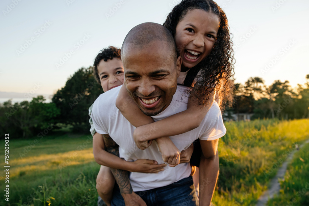 Playful family wrestling with piggy backs outside.