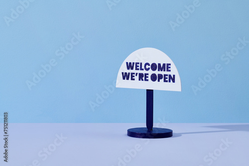 Welcome we are open signage hanging on pastel color background photo