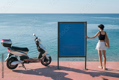 Young woman stands near an advertising stand on the seafront. 