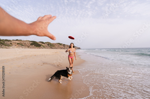 woman throwing a frisbee at a person on the beach with her dog. photo