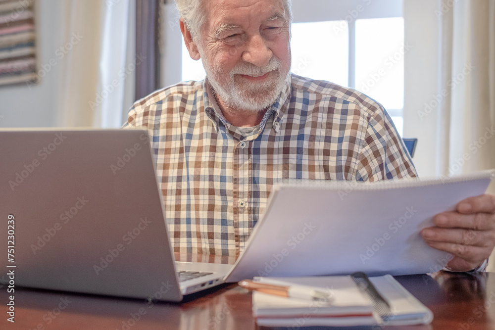 Smiling bearded man sitting at table with laptop and books working or studying. Attractive senior man enjoying teaching activity and learning using new technology Smiling bearded man sitting at table with laptop and books working or studying. Attractive senior man enjoying teaching activity and learning using new technology