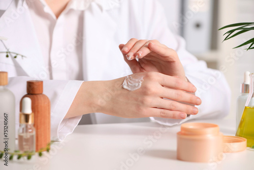 Dermatologist applying cream onto hand at white table indoors, selective focus. Testing cosmetic product