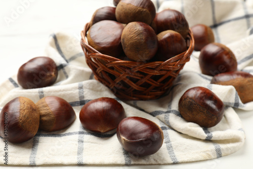 Sweet fresh edible chestnuts in wicker bowl on white table, closeup