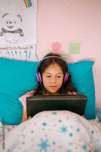 A little girl is looking at an electronic tablet lying in her bed  photo