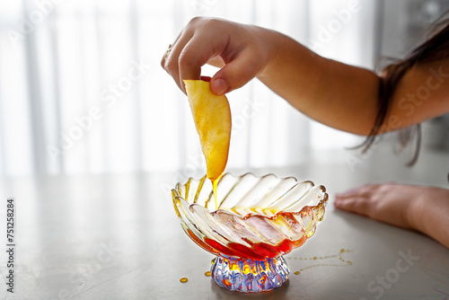 Rosh Hashanah Sweet Tradition. Young Girl's Hand Dips Apple in Honey. photo
