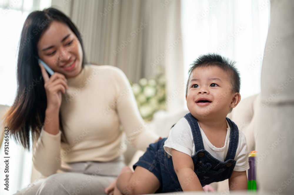 A cute Asian baby boy is crawling in the living room while his mom is talking on the phone. A cute Asian baby boy is crawling in the living room while his mom is talking on the phone.