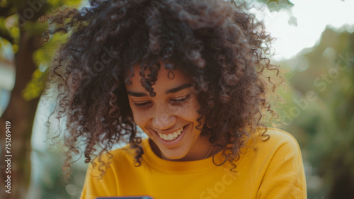Joyful woman with curly hair smiling down at her smartphone, immersed in a message.