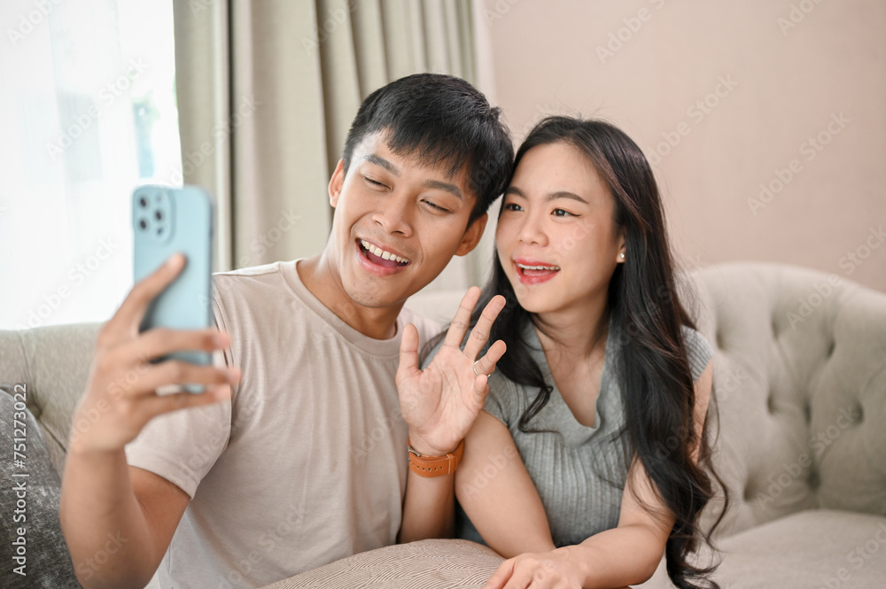Lovely Asian couple taking selfies with a smartphone together while relaxing in the living room. Lovely Asian couple taking selfies with a smartphone together while relaxing in the living room.