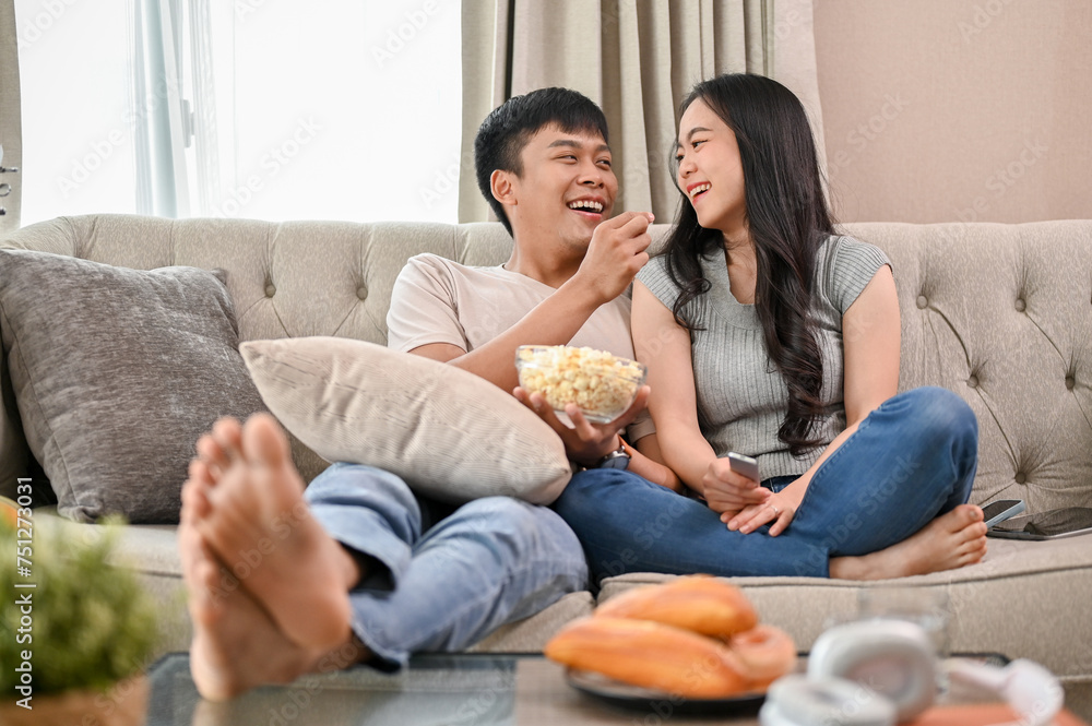 Happy young Asian couple enjoy eating popcorn and watching a movie while relaxing on a sofa. Happy young Asian couple enjoy eating popcorn and watching a movie while relaxing on a sofa.
