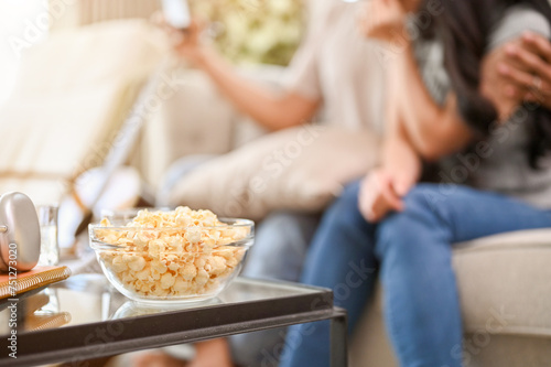 A popcorn bowl on a coffee table in the living room with a lovely couple sitting on a sofa.