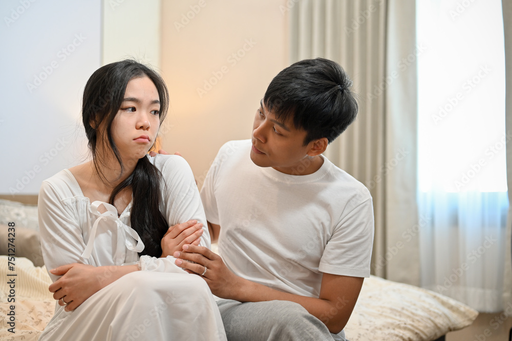 A man apologizes, asking for forgiveness from his sad girlfriend after their argument in the bedroom A man apologizes, asking for forgiveness from his sad girlfriend after their argument in the bedroom