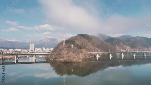 The cloudy mountains and numerous bridges crossing in front of them are reflected in the lake.