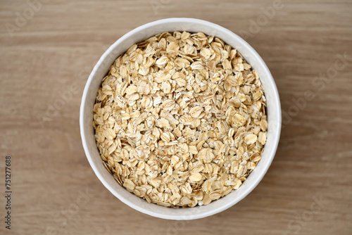 Dry rolled oat flakes oatmeal in plate on wooden table, top view