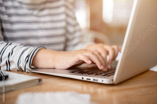 A close-up shot of a woman working on her laptop computer at her desk  typing on laptop keyboard.