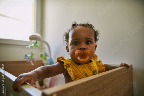 A baby toddler girl holding herself up while inside her crip photo
