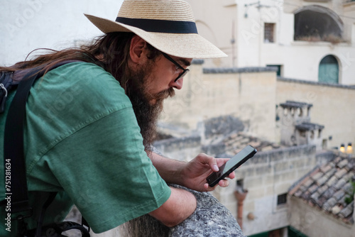 Bearded male tourist with hat using mobile phone in Matera, Italy photo