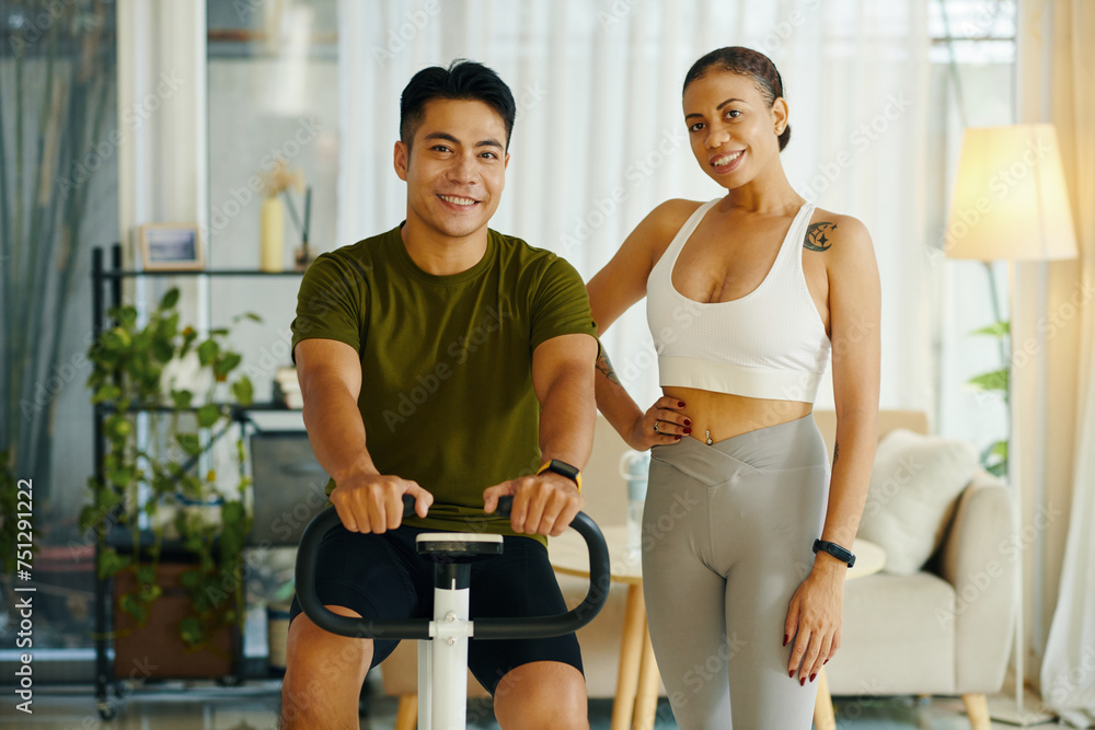 Fit smiling diverse couple exercising on bike at home Fit smiling diverse couple exercising on bike at home