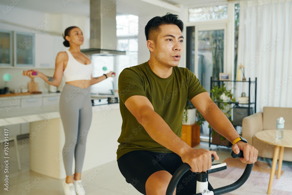 Fit man riding exercise bike when his girlfriend jumping with skipping rope Fit man riding exercise bike when his girlfriend jumping with skipping rope