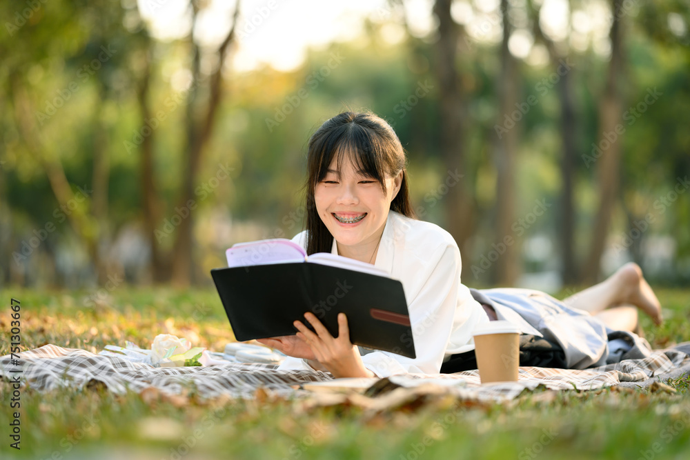 Cheerful young Asian woman lying down on green grass and reading a book Cheerful young Asian woman lying down on green grass and reading a book