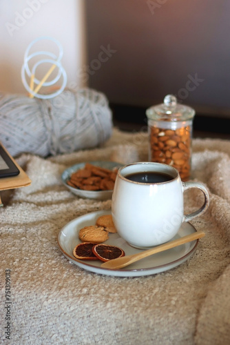 Cup of tea or coffee, cookies, books, glasses, e-reader, almonds, ball of yarn, knitting needles and lit candles on the table. Hygge at home. Selective focus.