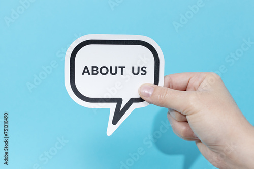 Hand holding speech bubble with text About Us isolated on blue background