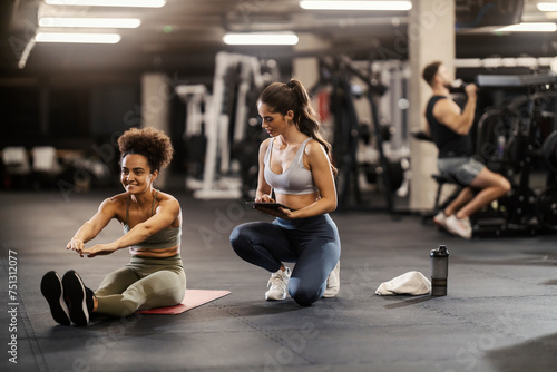 A sportswoman is sitting on a mat and exercising. Personal trainer is tracking her progress.