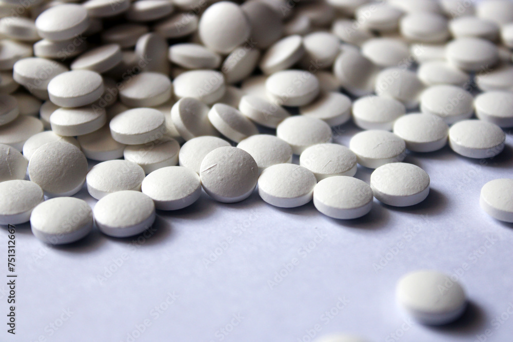 A lot of white pills are scattered on a white background. A lot of white pills are scattered on a white background.