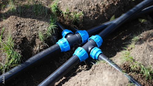 Black long pipe lies and tee adapter in dug-out earth closeup. Watering system in garden