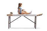 Full length profile shot of a child with leg injury sitting on a phycical therapy bed