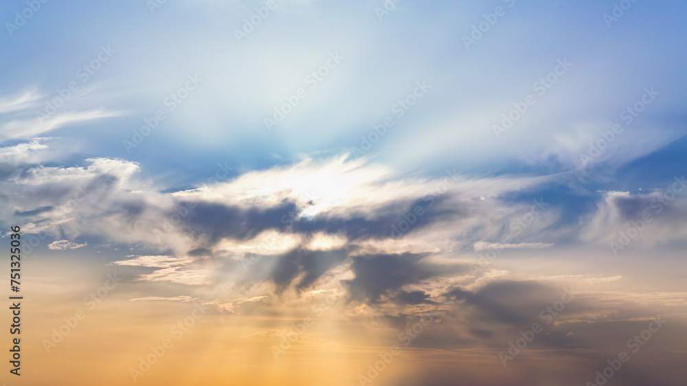 Serene sky scene with sun rays piercing through a central cloud, casting a warm glow on the surrounding clouds against a blue backdrop