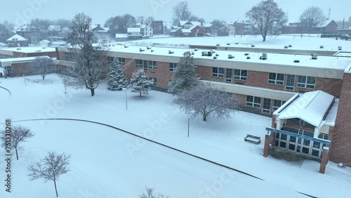 American public school during blizzard. Education building closed during snow storm. Aerial of brick school.
