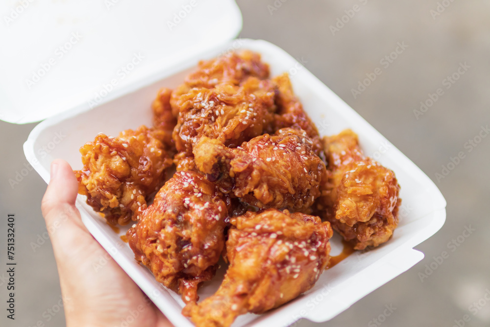 Hand holding deep fried chicken wing with spicy korean sauce in paper box package with street background. Hand holding deep fried chicken wing with spicy korean sauce in paper box package with street background.
