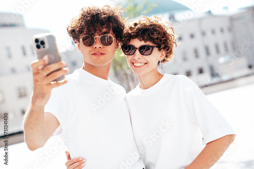 Young smiling beautiful woman and her handsome boyfriend in casual summer white t-shirt and jeans clothes. Happy cheerful family. Female having fun. Couple posing in street at sunny day. Take selfie