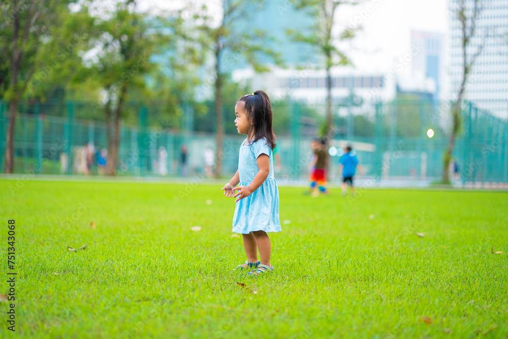 Adorable toddler asian girl enjoying walk and run on green grass in city park sunset light