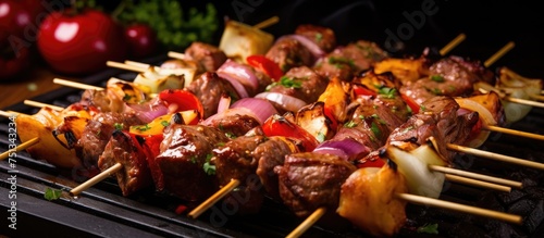 A close-up view of a skewer of food grilling on a hot grill. The skewer appears to be loaded with juicy meat and vegetables cooking over an open flame.