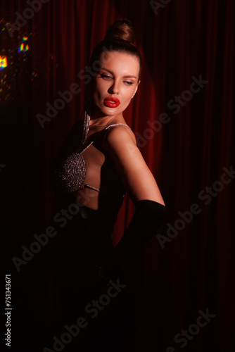 Gorgeous brunette woman in short black dress. Round light. Cabare style, St Valentines's Day. Beautiful lady with great make-up, big red lips, sparkling earrings portrait. Red curtains background