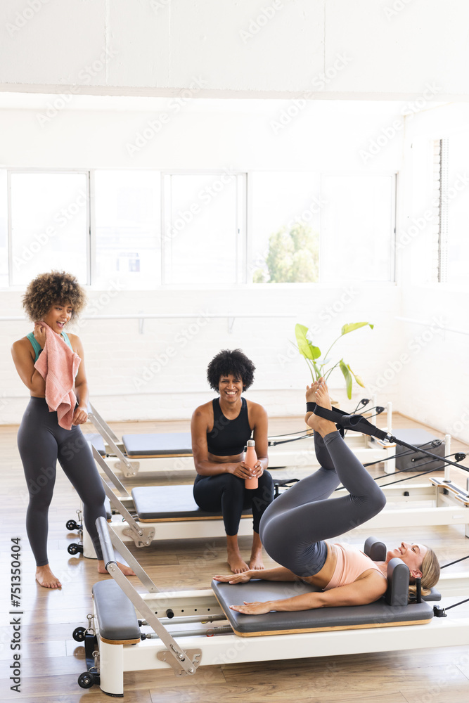 Biracial women exercising on Pilates reformers in a bright fitness studio with copy space Biracial women exercising on Pilates reformers in a bright fitness studio with copy space