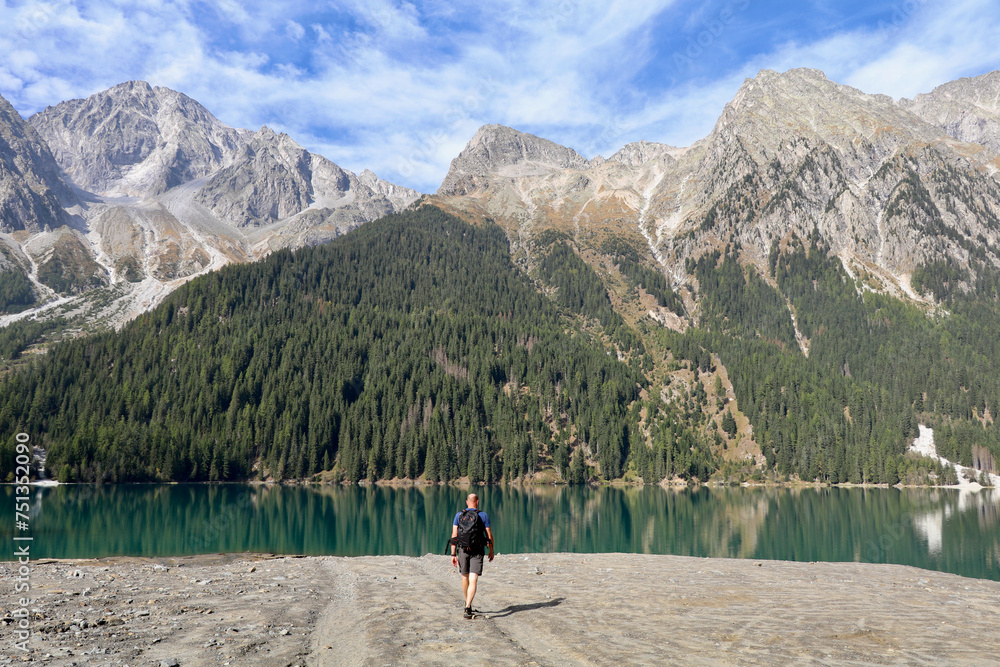 hiker on walking towards an emerald green mountain lake surrounded by high alpine mountains hiker on walking towards an emerald green mountain lake surrounded by high alpine mountains