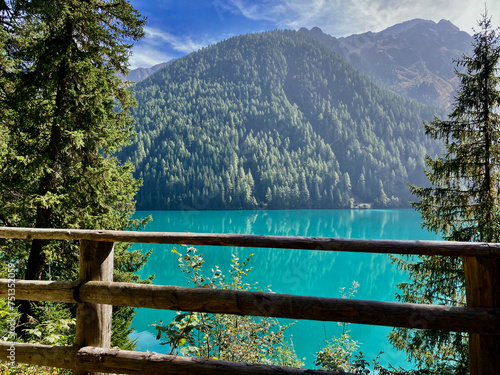 emerald green water of Lake Antholz and high mountains seen through the coniferous trees of the surrounding forest  photo