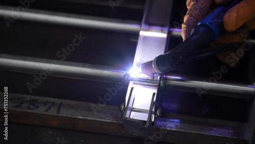 A blacksmith welder in a protective mask is seen working with metal steel and iron using a welding machine, with bright sparks and flashes captured in extreme slow motion