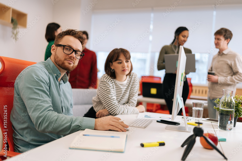 Handsome businessman looking at camera while sitting in boardroom on meeting. Diverse businesspeople negotiating on blurred background. Corporate business collaboration concept. Handsome businessman looking at camera while sitting in boardroom on meeting. Diverse businesspeople negotiating on blurred background. Corporate business collaboration concept.