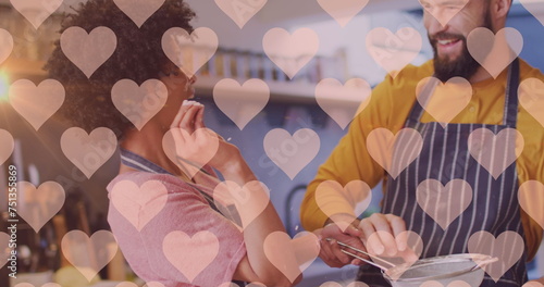 Image of hearts over diverse couple preparing meal in kitchen