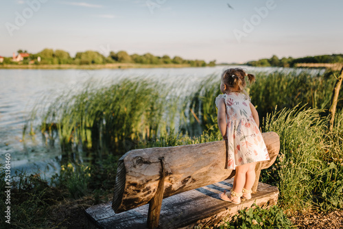 Obraz na plátne Kid on a bench on the shore of the lake at sunset