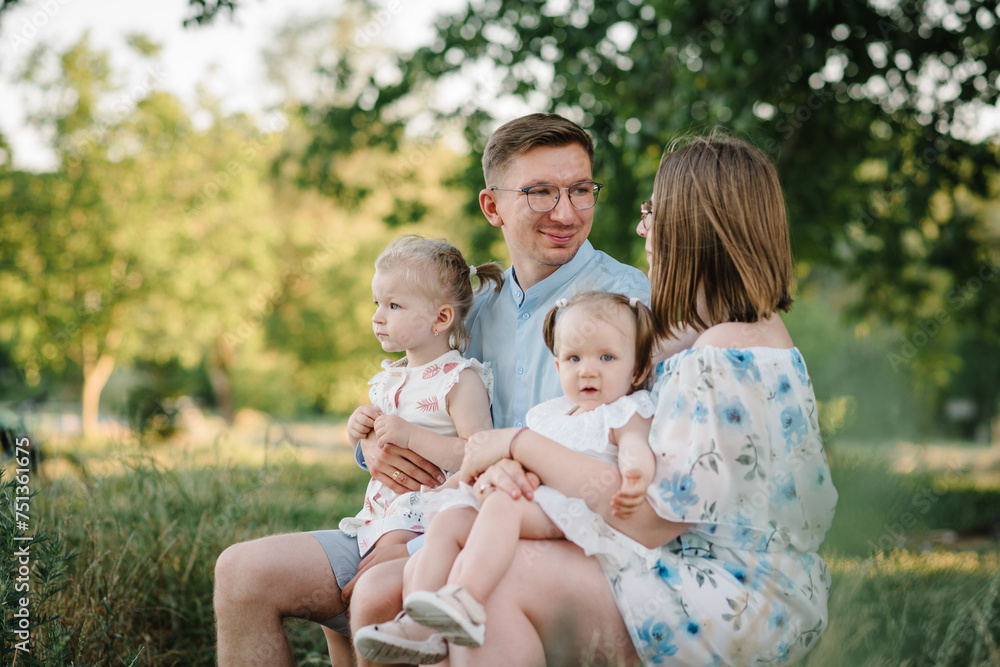 A loving couple with two childs. Mother, father embrace kids and spend time together. A happy family is sitting on bench on shore of lake at sunset. Mom, dad hug children daughter in the summer park. A loving couple with two childs. Mother, father embrace kids and spend time together. A happy family is sitting on bench on shore of lake at sunset. Mom, dad hug children daughter in the summer park.