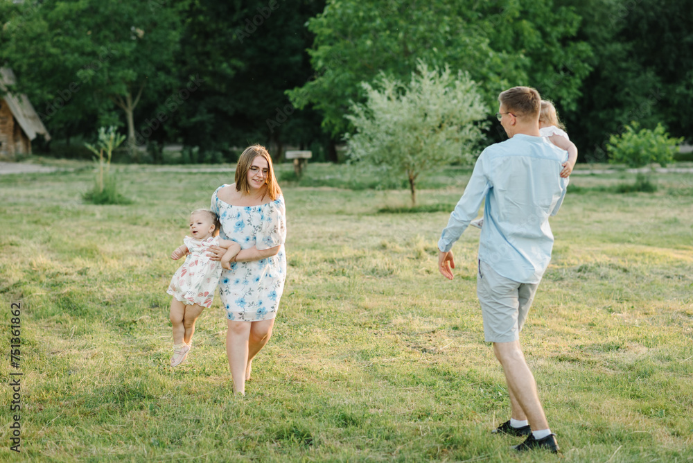 Concept of family spending time together. Mother, father hold hands children daughter. Running in green grass in nature on summer day. Mom, dad, and kids walking in park at sunset. Spring vacation.