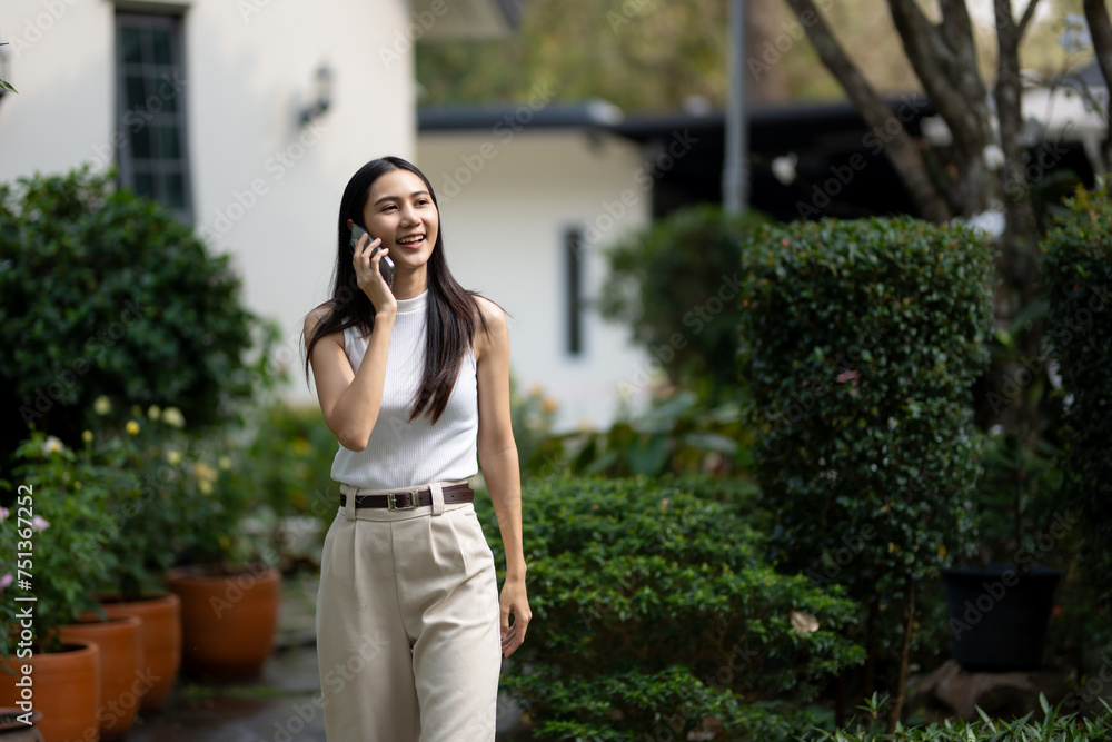 Cheerful young woman walks and talking on smartphone in lush green garden Cheerful young woman walks and talking on smartphone in lush green garden
