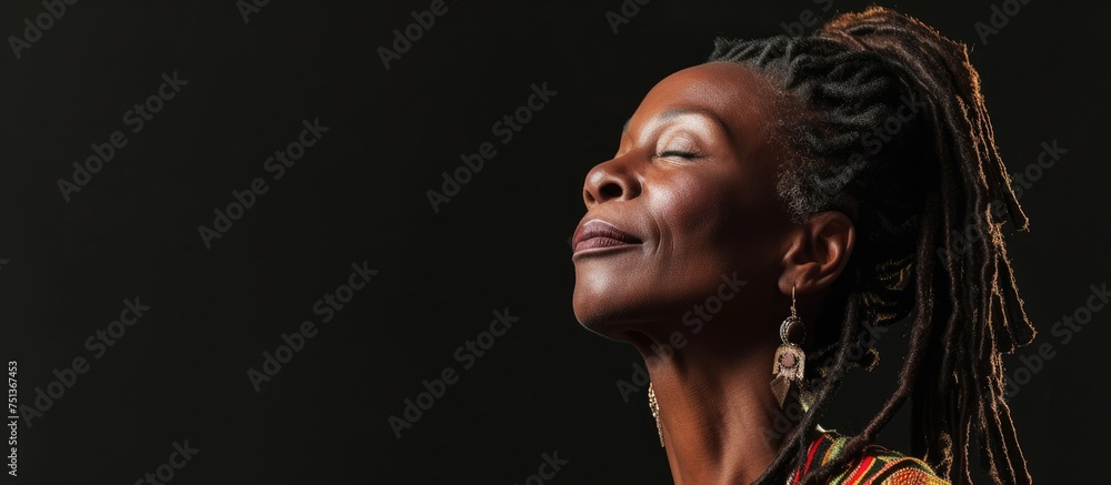 A confident and mature Black woman with dreadlocks is looking up into the sky, embracing her smooth dark skin. A confident and mature Black woman with dreadlocks is looking up into the sky, embracing her smooth dark skin.
