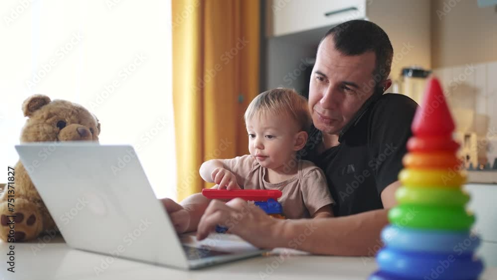 father working from home a remotely with baby son in his arms. pandemic remote work business concept. father tries to work at home in kitchen, baby children interfere fun sitting on their hands father working from home a remotely with baby son in his arms. pandemic remote work business concept. father tries to work at home in kitchen, baby children interfere fun sitting on their hands