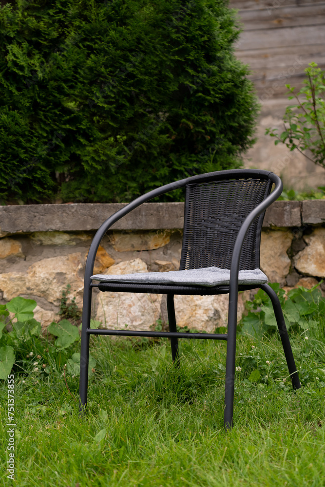 Wicker rattan chair stands in summer garden on background of stone fence. Garden furniture Wicker rattan chair stands in summer garden on background of stone fence. Garden furniture