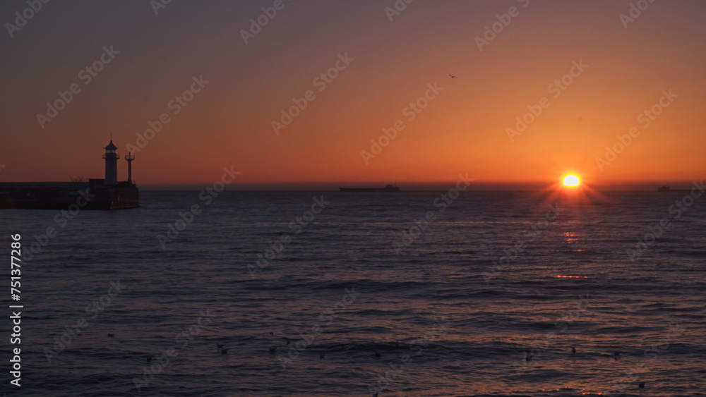 Sunrise at sea. Ships and a lighthouse can be seen on the horizon